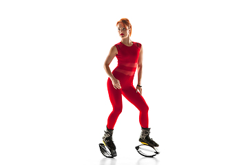 Image showing Beautiful redhead woman in a red sportswear jumping in a kangoo jumps shoes isolated on white studio background.