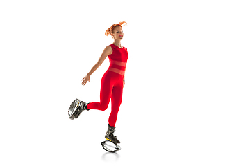 Image showing Beautiful redhead woman in a red sportswear jumping in a kangoo jumps shoes isolated on white studio background.