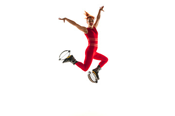 Image showing Beautiful redhead woman in a red sportswear jumping in a kangoo jumps shoes isolated on white studio background.