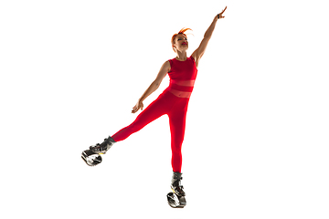 Image showing Beautiful redhead woman in a red sportswear jumping in a kangoo jumps shoes isolated on white studio background.