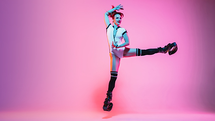 Image showing Beautiful redhead woman in a white sportswear jumping in a kangoo jumps shoes isolated on gradient studio background in neon light