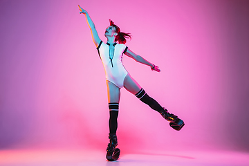 Image showing Beautiful redhead woman in a white sportswear jumping in a kangoo jumps shoes isolated on gradient studio background in neon light