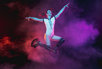 Image showing Beautiful redhead woman in a white sportswear jumping in a kangoo jumps shoes isolated on gradient studio background in neon lighted smoke