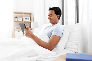 Image showing happy indian man with tablet pc in bed at home