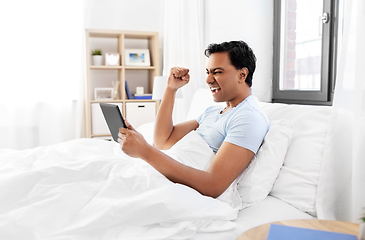 Image showing happy indian man with tablet pc in bed at home