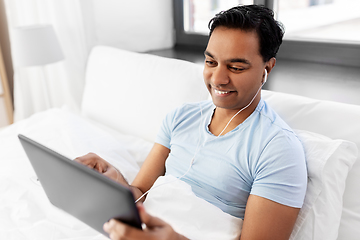 Image showing happy indian man with tablet pc in bed at home