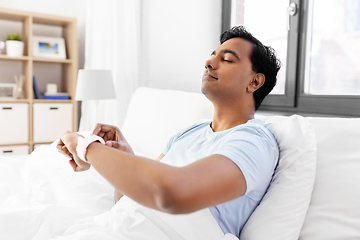 Image showing happy indian man with smart watch in bed at home