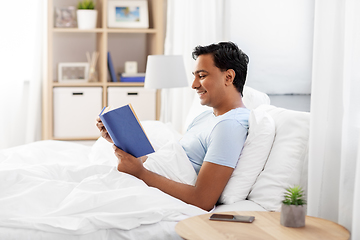 Image showing happy indian man reading book in bed at home