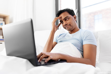 Image showing bored indian man with laptop in bed at home