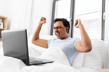 Image showing happy indian man with laptop in bed at home