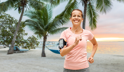 Image showing woman with earphones add armband jogging at park