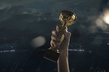 Image showing Award of victory, male hands tightening the cup of winners against cloudy dark sky