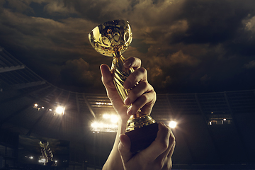 Image showing Award of victory, male hands tightening the cup of winners against cloudy dark sky