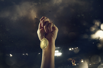 Image showing Award of victory, male hands tightening the medal of winners against cloudy dark sky