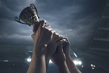 Image showing Award of victory, male hands tightening the cup of winners against cloudy dark sky