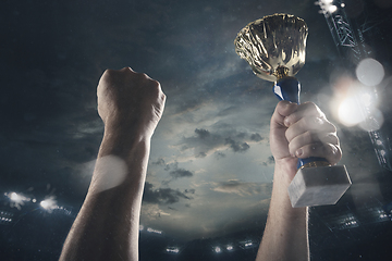 Image showing Award of victory, male hands tightening the cup of winners against cloudy dark sky