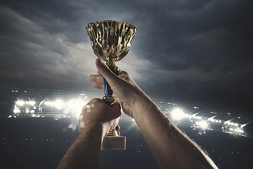 Image showing Award of victory, male hands tightening the cup of winners against cloudy dark sky