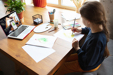 Image showing Girl drawing with paints and pencils at home, watching teacher\'s tutorial on laptop. Digitalization, remote education