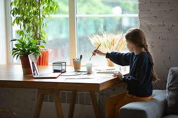 Image showing Girl drawing with paints and pencils at home, watching teacher\'s tutorial on laptop. Digitalization, remote education