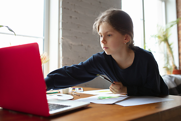 Image showing Girl drawing with paints and pencils at home, watching teacher\'s tutorial on laptop. Digitalization, remote education