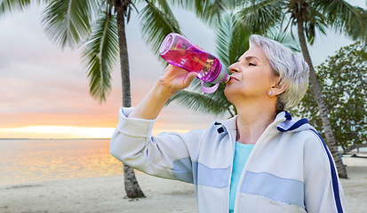 Image showing senior woman drinks water after exercising in park