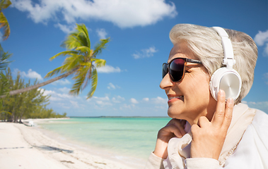 Image showing old woman in headphones listens to music on beach