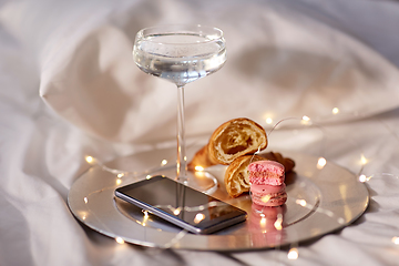 Image showing champagne glass, croissants and smartphone in bed