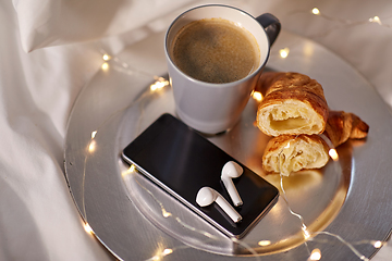 Image showing smartphone, earphones, coffee and croissant in bed