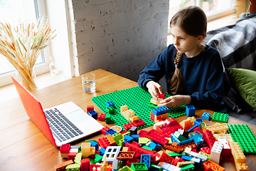 Image showing Girl playing with constructor at home, watching teacher\'s tutorial on laptop. Digitalization, remote education