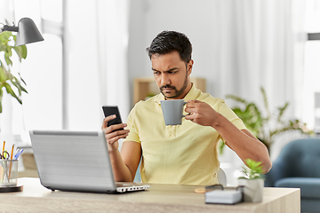 Image showing man with smartphone drinking coffee at home office