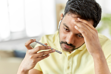 Image showing stressed man with earphones calling on smartphone