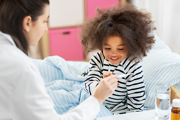 Image showing doctor showing thermometer to smiling sick girl