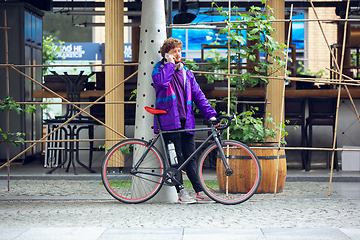 Image showing Handsome young man using mobile phone and headphones while standing near his bicycle beside him