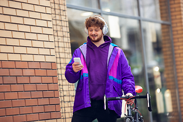 Image showing Handsome young man using mobile phone and headphones while standing near his bicycle beside him