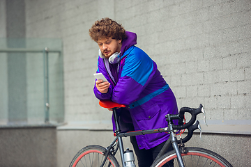 Image showing Handsome young man using mobile phone and headphones while standing near his bicycle beside him