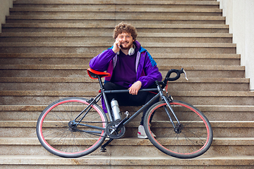 Image showing Handsome young man using mobile phone and headphones while sitting near his bicycle beside him