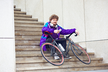 Image showing Handsome young man using mobile phone and headphones while sitting near his bicycle beside him