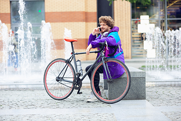 Image showing Handsome young man using mobile phone and headphones while sitting near his bicycle beside him