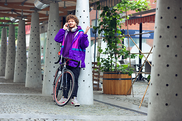 Image showing Handsome young man using mobile phone and headphones while standing near his bicycle beside him