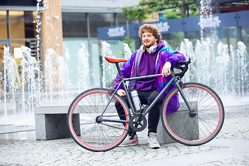 Image showing Handsome young man using headphones while sitting near his bicycle beside him