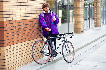 Image showing Handsome young man using mobile phone and headphones while standing near his bicycle beside him