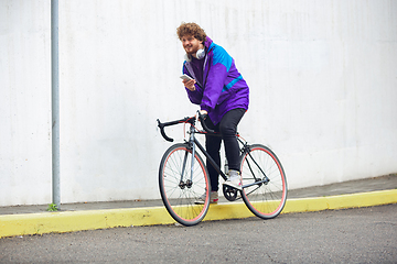 Image showing Handsome young man using mobile phone and headphones while riding his bicycle