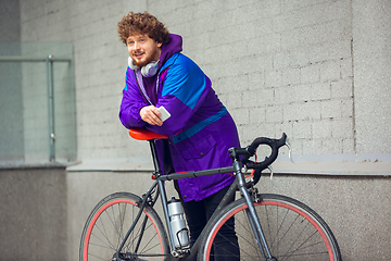 Image showing Handsome young man using mobile phone and headphones while standing near his bicycle beside him