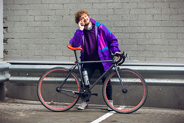 Image showing Handsome young man using mobile phone and headphones while standing near his bicycle beside him