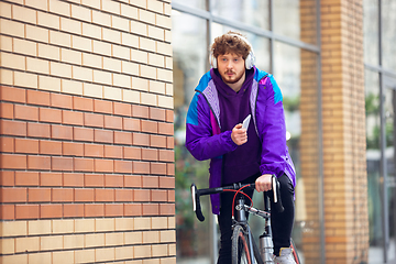 Image showing Handsome young man using mobile phone and headphones while riding his bicycle