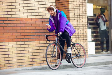 Image showing Handsome young man using mobile phone and headphones while riding his bicycle
