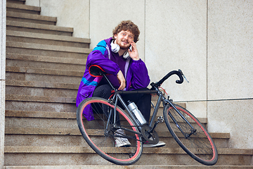 Image showing Handsome young man using mobile phone and headphones while sitting near his bicycle beside him