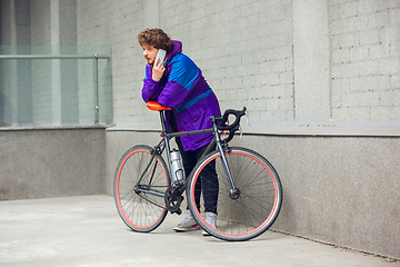 Image showing Handsome young man using mobile phone and headphones while standing near his bicycle beside him