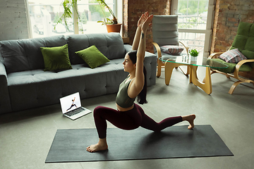 Image showing Sporty young woman taking yoga lessons online and practice at home