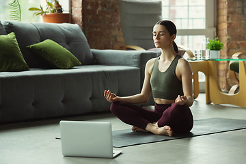 Image showing Sporty young woman taking yoga lessons online and practice at home